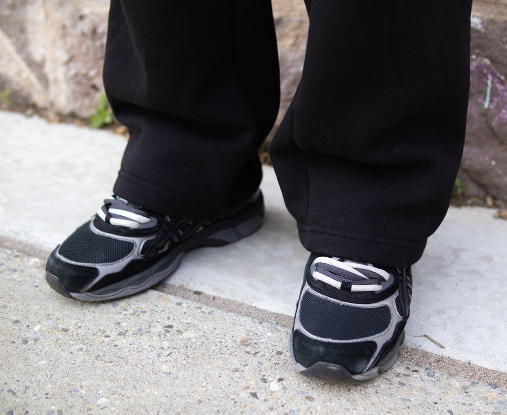 Person wearing black and gray sneakers on a concrete surface with a stone wall in the background